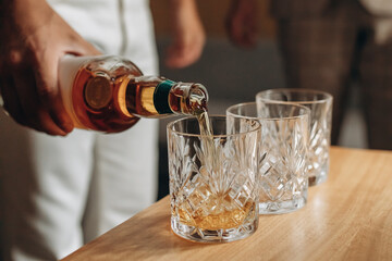 The man pours alcohol into a glass. Close photo of whiskey and scotch glasses. The guy holds a bottle in his hand