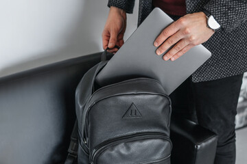 Man hand pulls a gray laptop with a black leather stylish backpack - obrazy, fototapety, plakaty