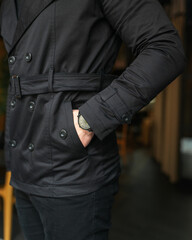 The man holds his hand in his pocket. Stylish men's clothing, pocket close up. Clock on hand on a trench coat background