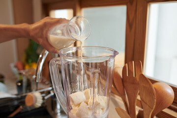 Man pouring non-diary milk in blender with cut bananas when making smoothie