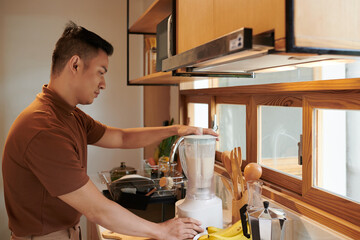 Vietnamese young man making banana smoothie for breakfast