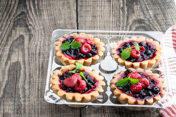 Delicious fruit tarts in plastic pack on wooden table