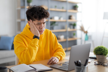 Bored Asian male student sitting at desk with pc