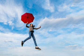 Little happy girl fly on background of blue cloudy sky holding red umbrella. Imagination,...