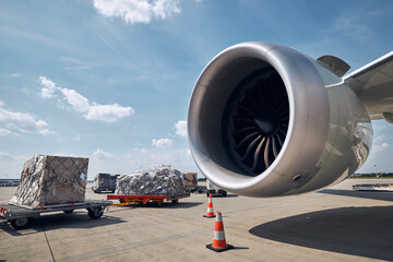 Preparation freight airplane at airport. Loading of cargo containers against jet engine of plane..