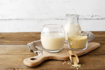 Millet milk in glass, jar and bowl on cutting board with wooden background