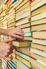 Female hand pulls a book from a big colored books stack in library background. knowledge in books is power.The girl сhose the book from many others vertical 