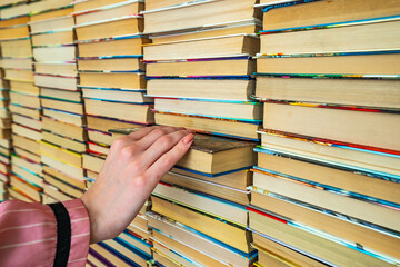 Female hand pulls a book from a big colored books stack in library background. knowledge in books is power.The girl in pink coatchooses take the book from many others