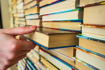 Female hand pulls a book from a big colored books stack in library background. knowledge in books is power.The girl chooses pulls the book from many others