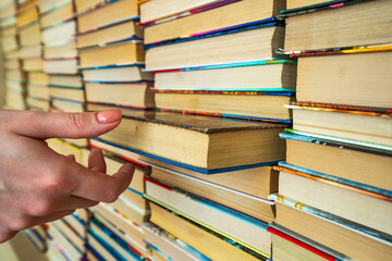 Many books in stacks and hand taking book from stack of books on the library background. knowledge in books is power. Many multicolored books in columns and Student Man hand