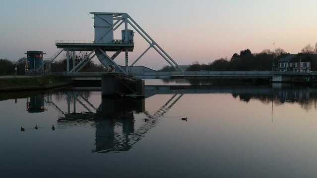 Coucher de soleil sur le rivi&egrave;re derri&egrave;re un pont avec des canards qui nagent