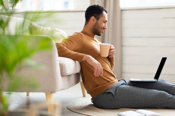 Smiling Arab man watching video on computer, drinking coffee