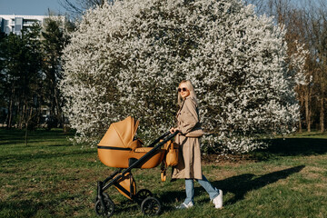 Blonde woman walking with a stroller in a park, smiling.