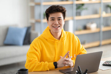 Condifent smiling Asian man posing sitting at desk