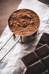 taza medidora de metal con cacao en polvo y una tableta de chocolate