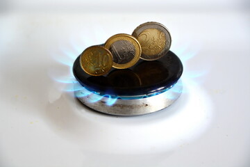 concept of natural gas price growth due to European crisis is euro coins on burning white gas stove hob blue flames, closeup