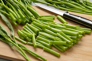 Fresh raw green pieces hollow water spinach,  kangkong, on a wooden cutting board close up 