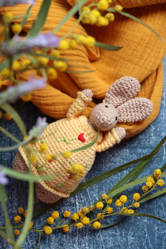 Crochet Easter bunny on grey background. Beautiful spring bouquet of mimosa and lavender flowers on a table. Hobbies and free time concept.  