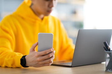 Asian man sitting at desk using cell phone, closeup