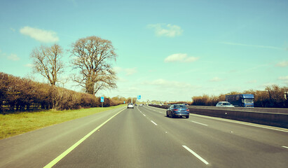 Rear view of cars driving on motorway, Ireland. Road with metal safety barrier or rail. cars on the asphalt under the cloudy blue sky. Highway traffic.
