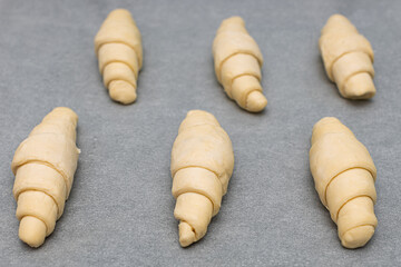 raw dough croissants lie on a baking sheet