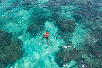 Topview an Asian man who Thumbing up to the camera and  are floating and snorkeling over the surface sea with life jacket on them.