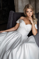 Happy feminine and stylish blonde bride posing near a large window, good mood. The girl in the chair