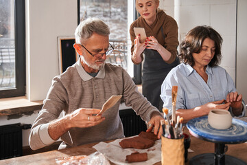Man holding wooden stack and looking at the clay while preparing making something from it