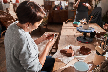 Woman sitting at the table and preparing making something from clay with special stick