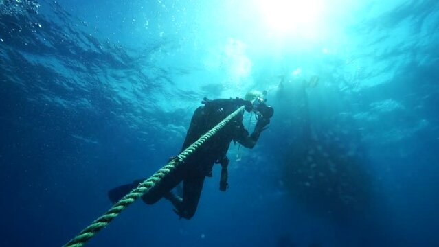 Image of photographer divers climbing aboard a rope underwater.