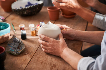Mature woman holding glaze brush and preparing using it on ceramic surface