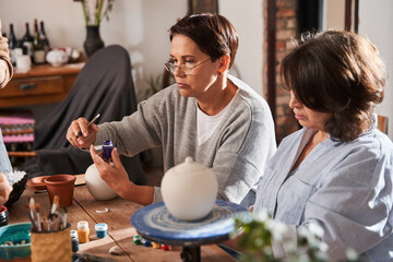 Mature woman holding glaze brush and opening paints