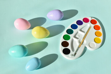 Paints and Easter painted eggs on a light blue background. Flat position, top view