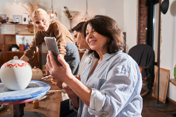 Woman taking photo of her clay pot at the smartphone after successful master class