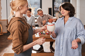 Senior woman giving hand made clay pot to her teacher after the master class