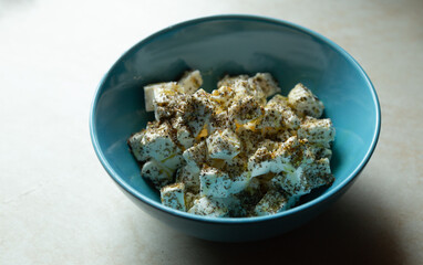 Traditional greek cuisine appetizer. Blue modern bowl filled with diced feta soft cheese, herb mix seasoning and olive oil. Handmade homecooked Mediterranean healthy meal. Top view copy space