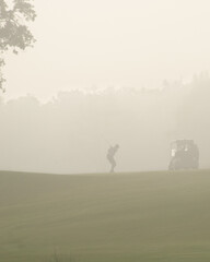 A lone golfer silhouetted on a misty morning getting ready to hit off the fairway.