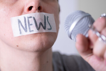 A man gags his mouth with duct tape saying news trying to speak into a microphone.