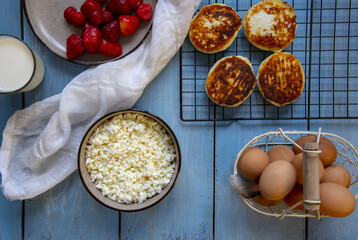 Cottage cheese, eggs, strawberries and cheesecakes on a blue countertop.