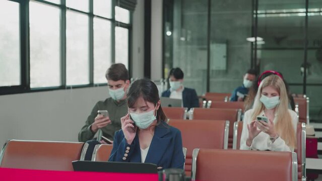 Airline passengers wear face masks sitting using smartphone and laptop while waiting for check-in at the airport. social distancing, New normal, Illness Prevention, Covid-19 concept