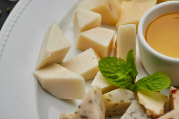 Cheese plate: Parmesan, cheddar, gouda, mozzarella and other with honey on white plate on dark background . Tasty appetizers. Top view. Photo for restaurant menu