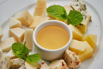 Cheese plate: Parmesan, cheddar, gouda, mozzarella and other with honey on white plate on dark background . Tasty appetizers. Top view. Photo for restaurant menu