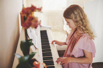 Portrait cute curly blond teenager girl playing keys piano at home bright interior