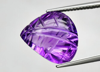 Natural gemstone purple amethyst in tweezers on a gray background