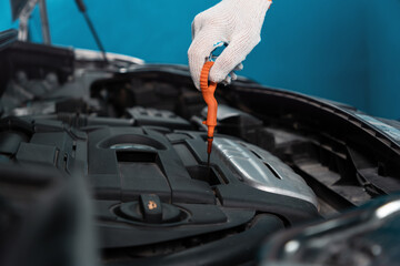 Close-up of a gloved hand pulling an oil dipstick out of the engine. The concept of car repair in an auto repair shop