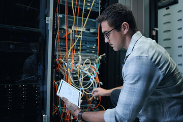 Running diagnostics. Cropped shot of a handsome young male programmer working on a tablet in a server room.