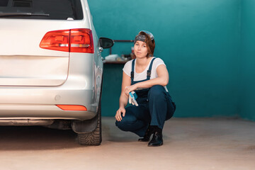 Young female mechanic is squatting near a car tire in an auto repair shop. The concept of women's work in male professions