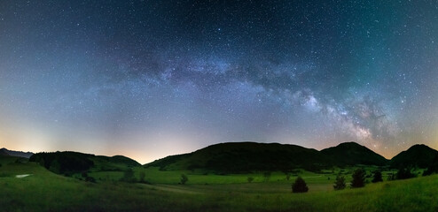 Panoramic night sky over Montelago highlands, Marche, Italy. The Milky Way galaxy arc and stars in unique hills landscape.