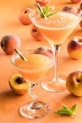 Two peach Bellinis surrounded by peaches against a peach background.