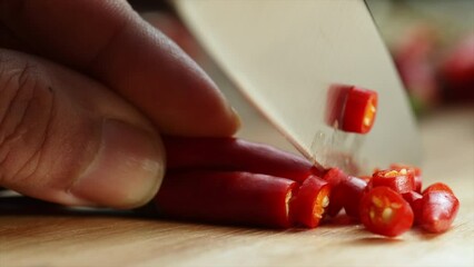 Slow motion close up of sharp chef knife slicing fresh red chili on wooden cutting board